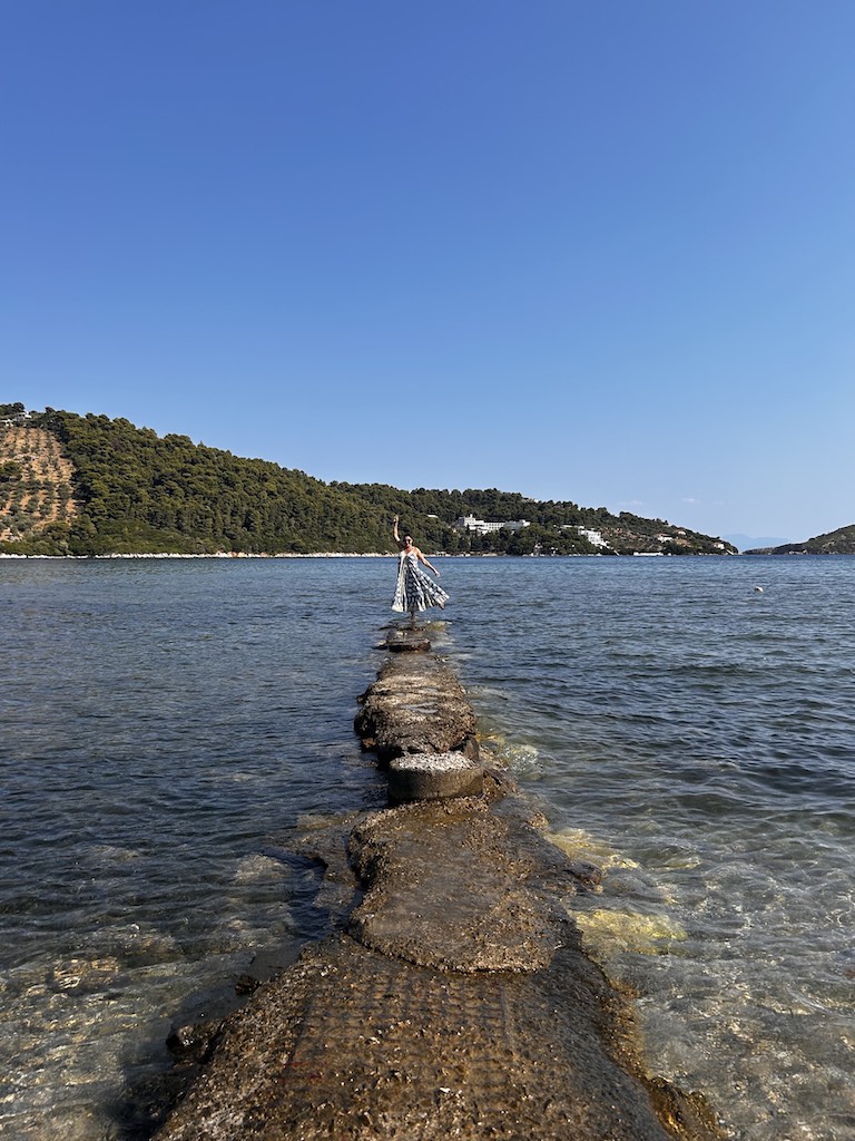 Eteri McKenzie walking confidently toward the horizon on a stone path surrounded by water, symbolising clarity, focus, and personal transformation.