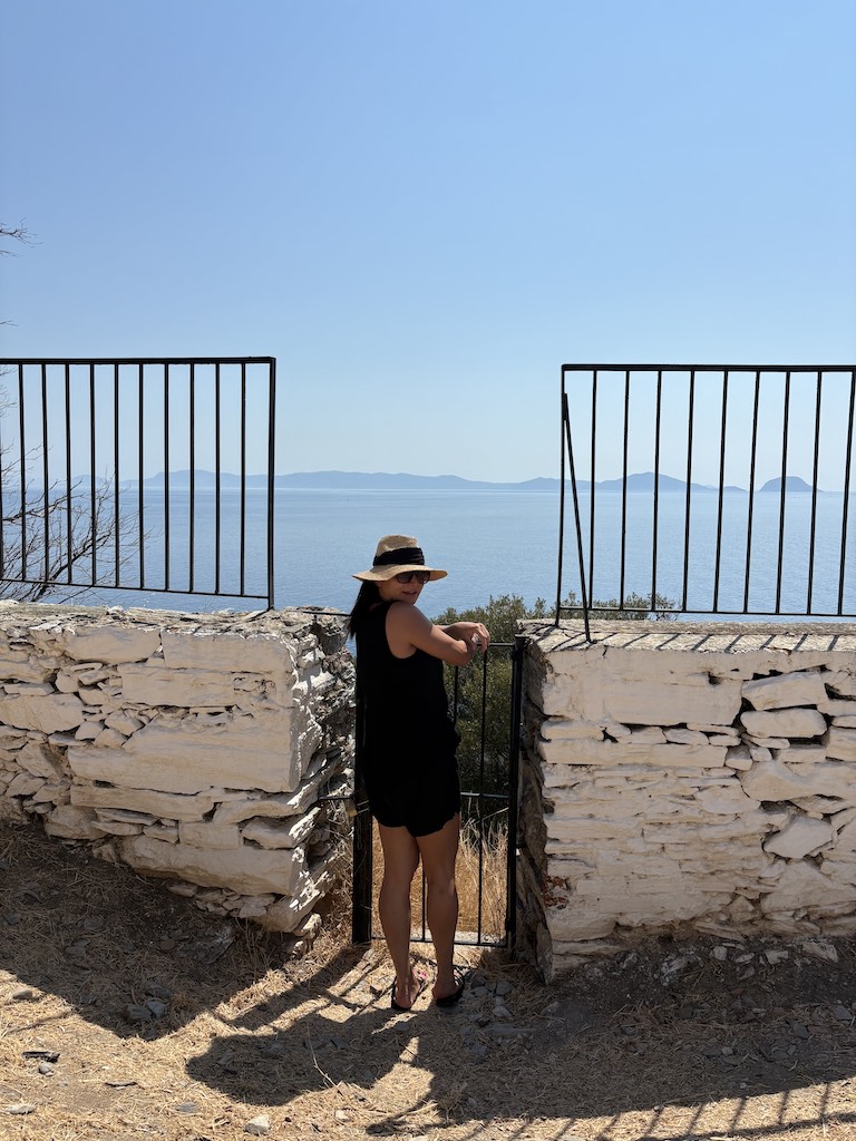 Eteri McKenzie standing in the sun against a stone wall and iron gate, symbolising strength and calm in the face of life's overwhelm.